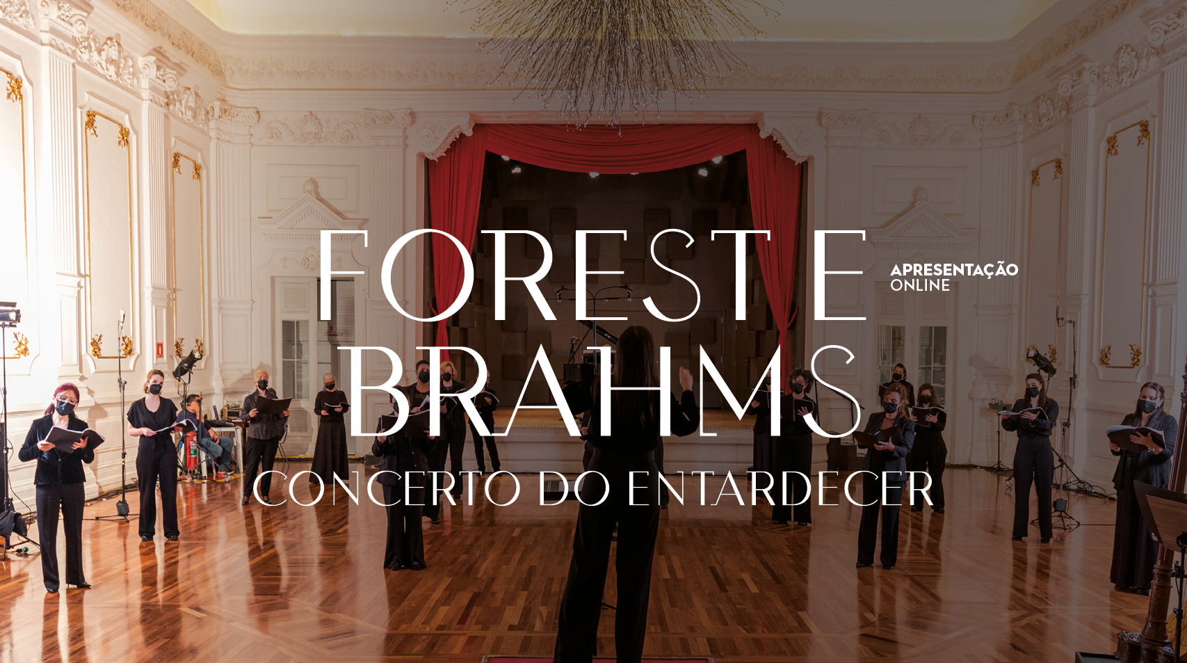 Sala do Conservatório, Praça das Artes. No centro da Imagem tem um pequeno palco com cortinas vermelhas, no teto tem um lustre semelhante a galhos de árvore e o texto "Foreste Brahms, Concerto do Entardecer". No canto superior direto, temos escrito "Apresentação online". Distribuída pela imagem temos mulheres de preto segurando partituras.
