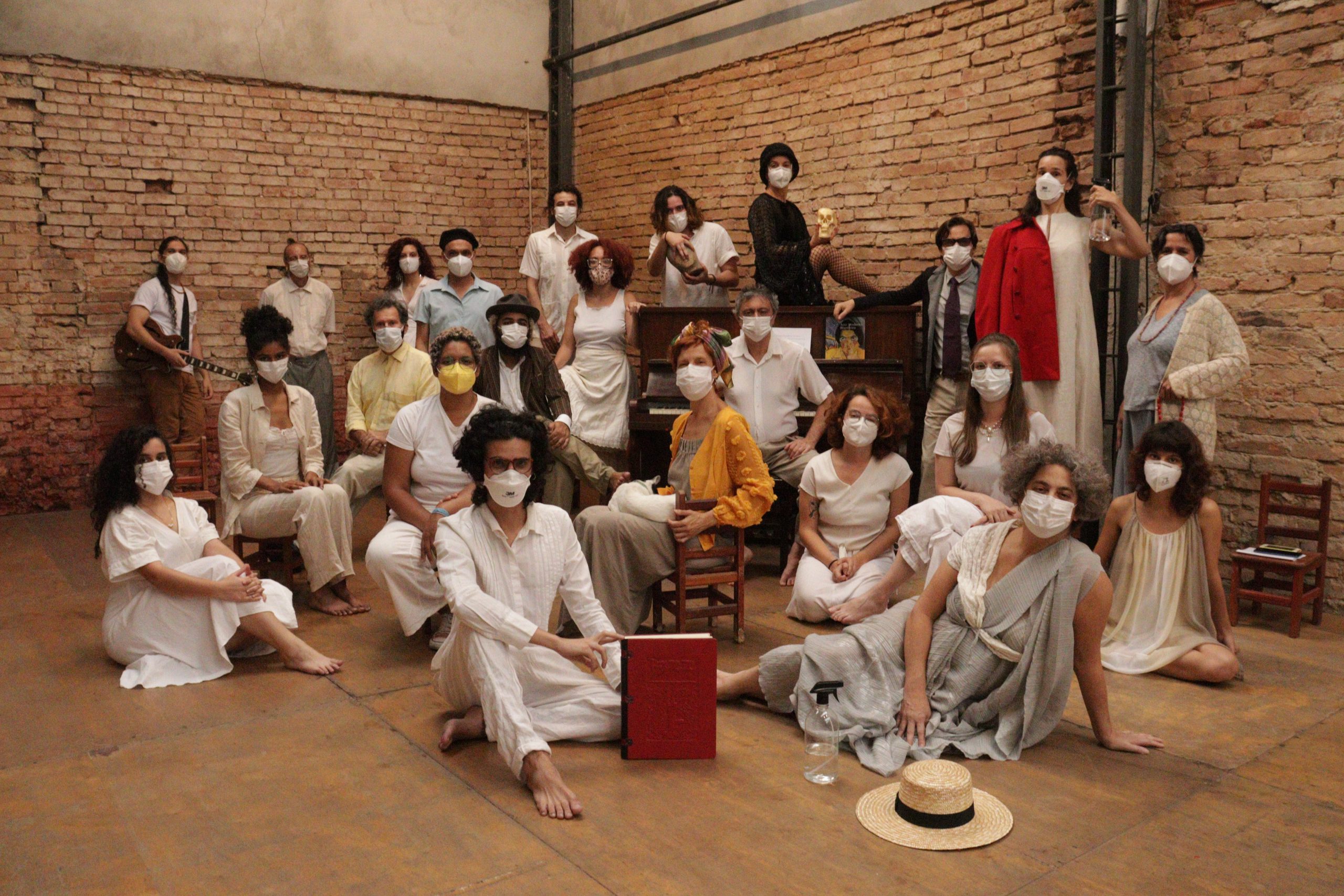Integrantes do grupo de teatro, todos com máscaras e roupas claras