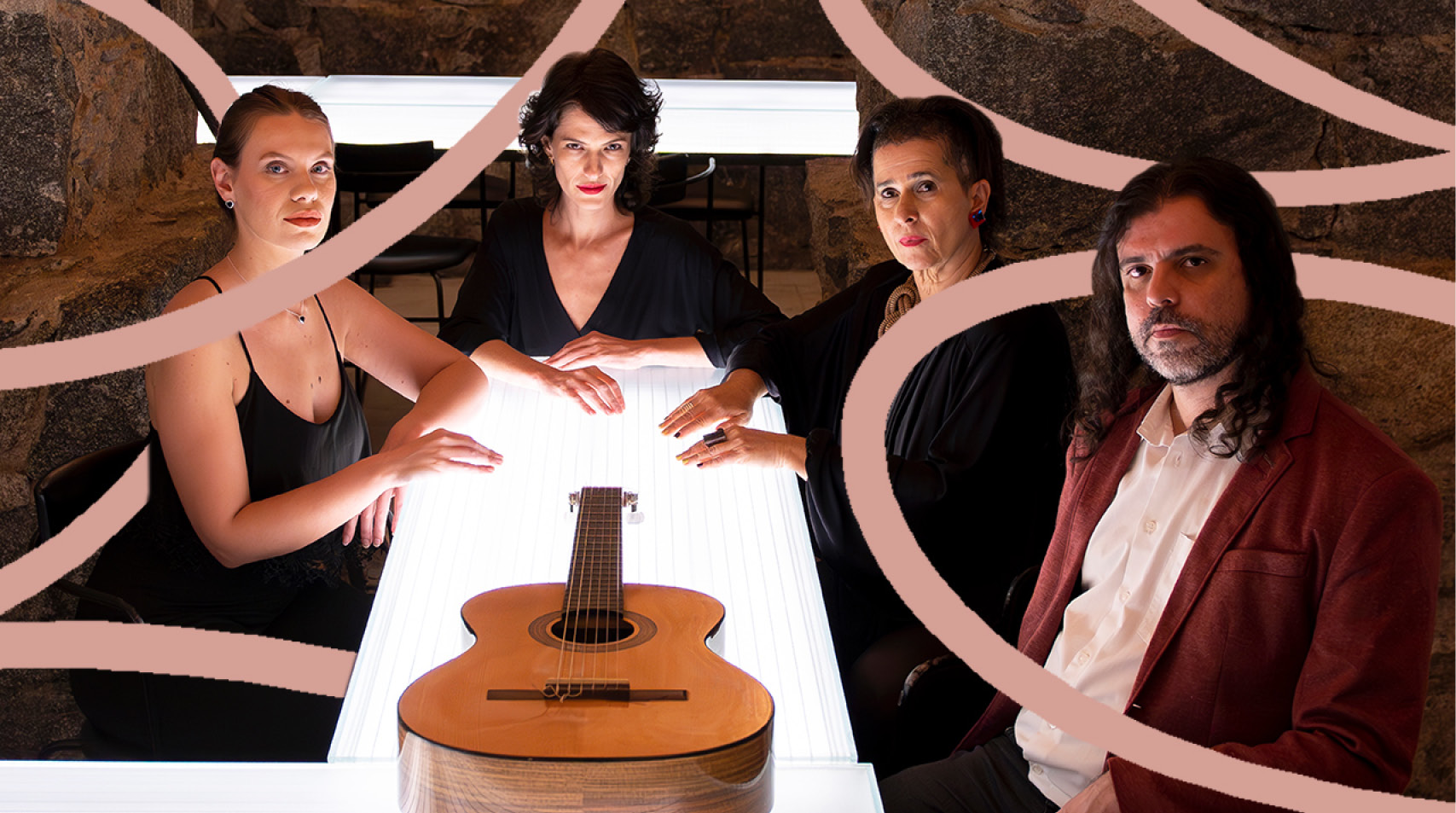 Foto de quatro artistas vestidos de preto olhando para a câmera numa mesa iluminada