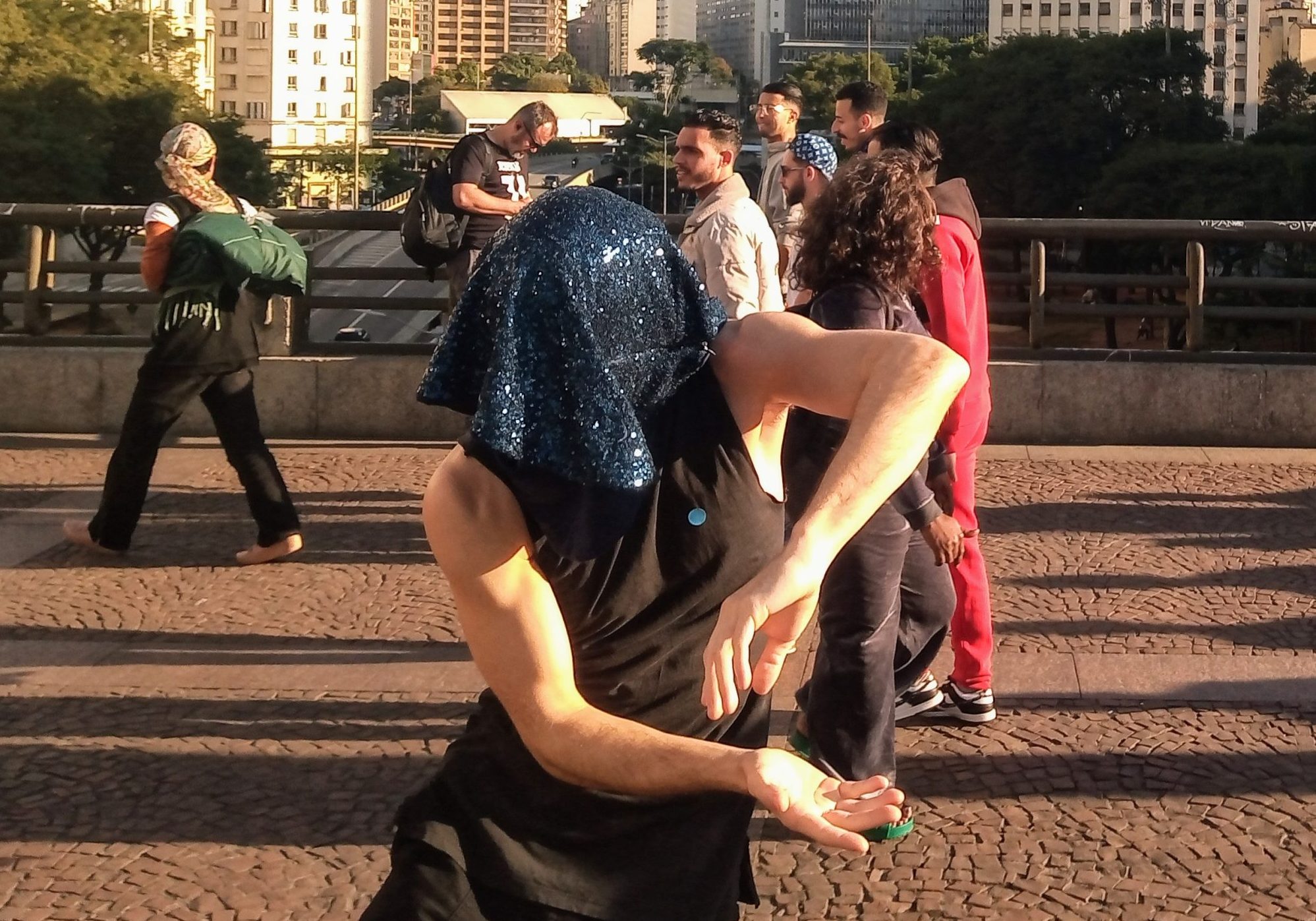 Artista com pano preto na cabeça performa em cima de um viaduto